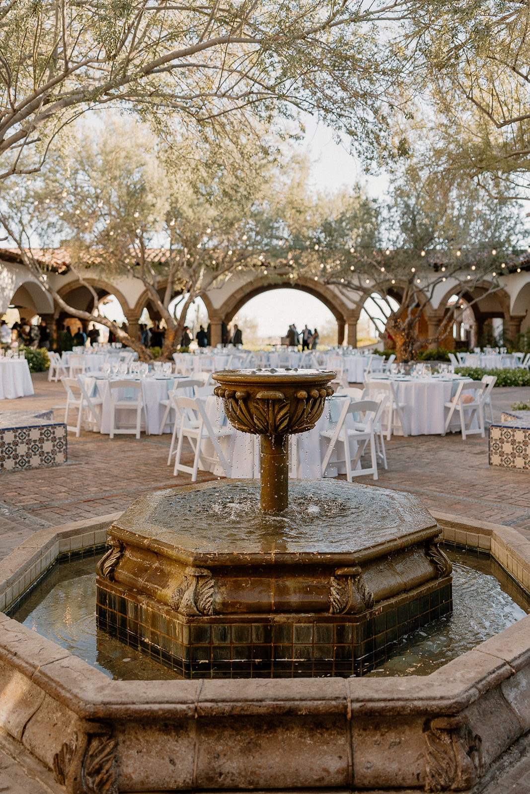 Outdoor reception setup at Blackstone Country Club with white tables and a rustic tile fountain in the foreground.