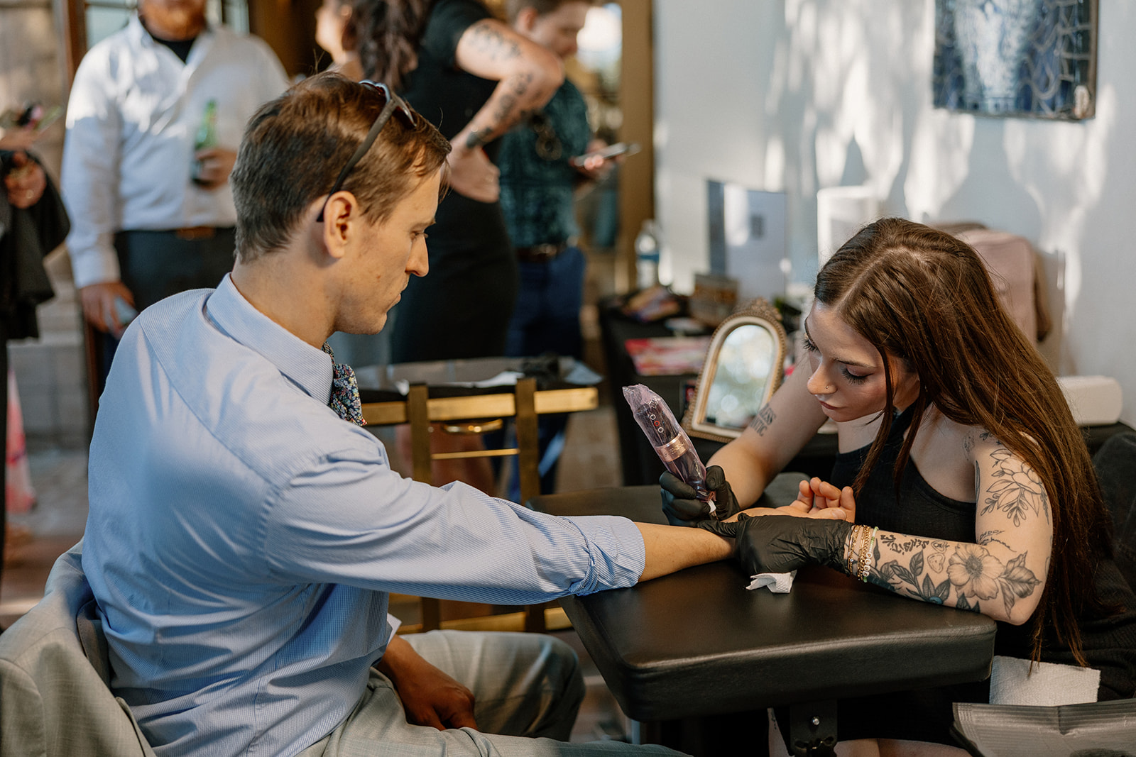 Wedding guest sits for a custom tattoo at Blackstone Country Club, with the artist working in the background of the lively reception.