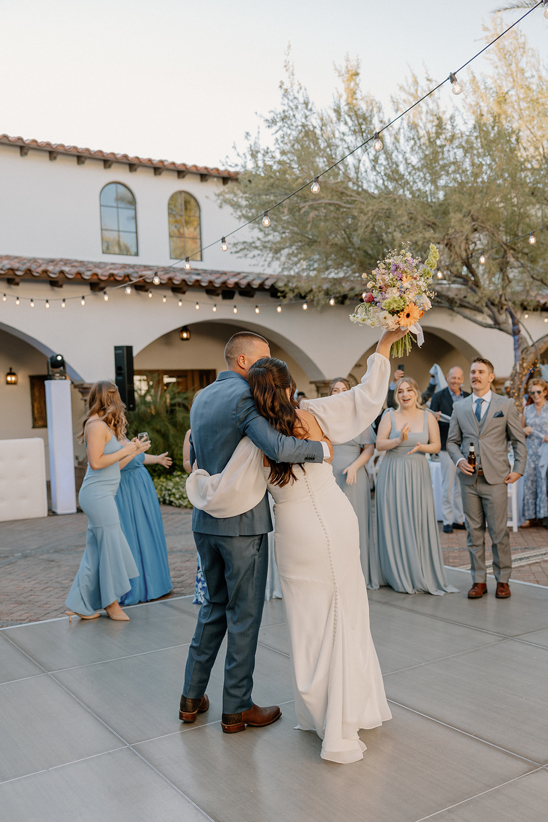 The bride raises her bouquet triumphantly as she and the groom kick off the reception on the dance floor, surrounded by cheering guests.