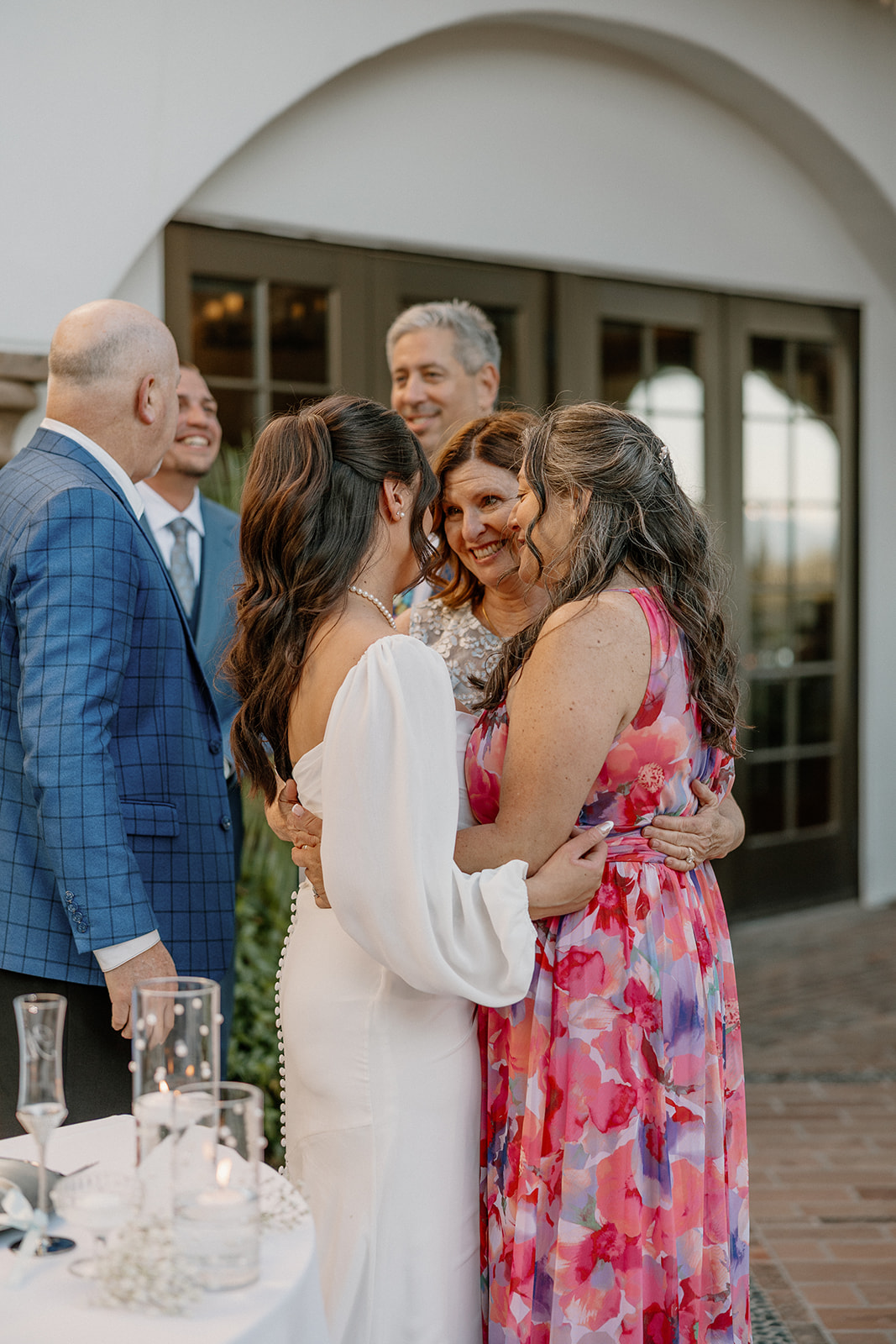 The bride shares a warm group hug with loved ones, surrounded by natural light and soft smiles during the cocktail hour.