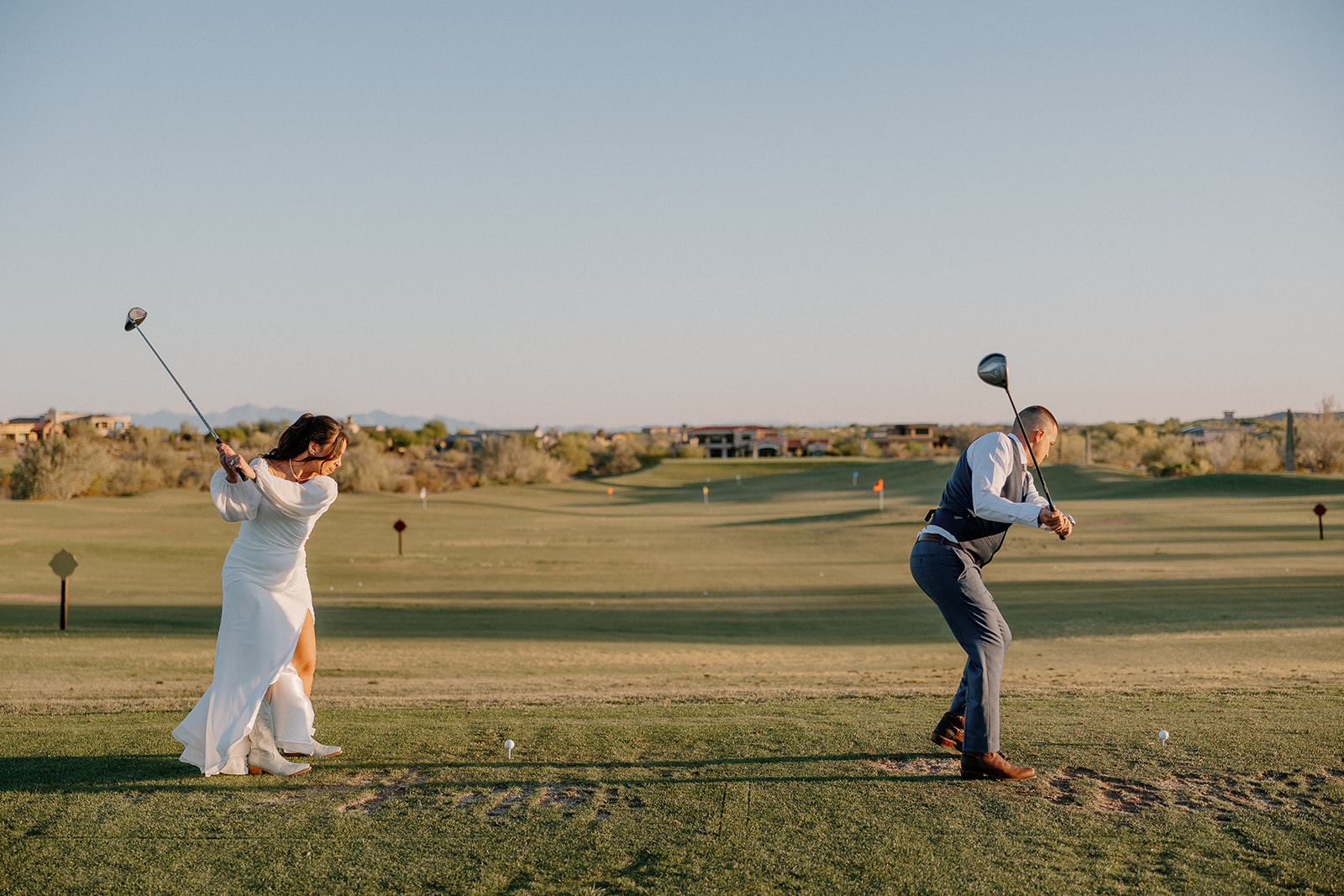 The bride and groom take a playful swing on the golf course at Blackstone Country Club—wedding attire meets tee time.