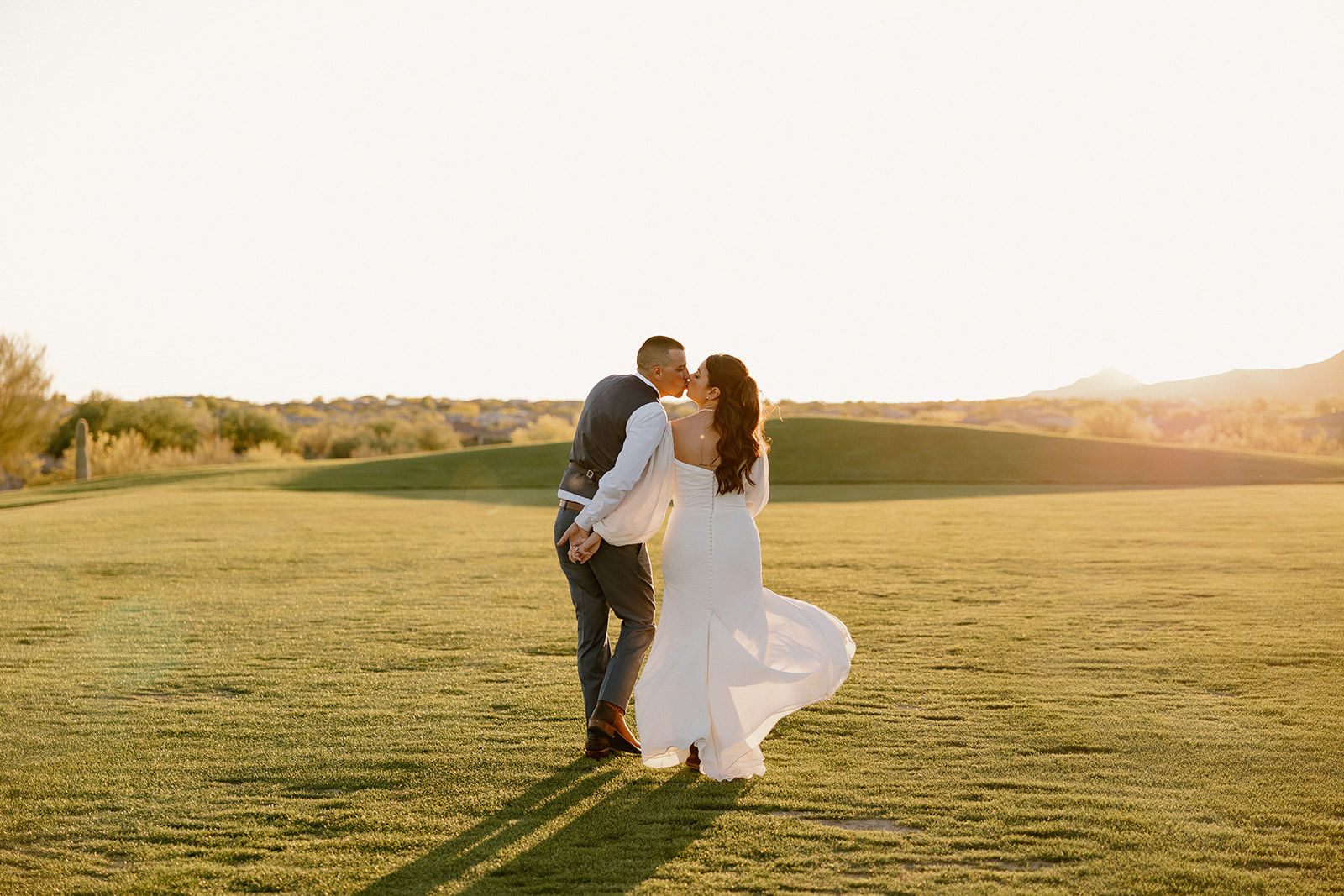 Bride and groom stroll across the Blackstone Country Club golf course, wrapped in each other as the sun sets behind them.