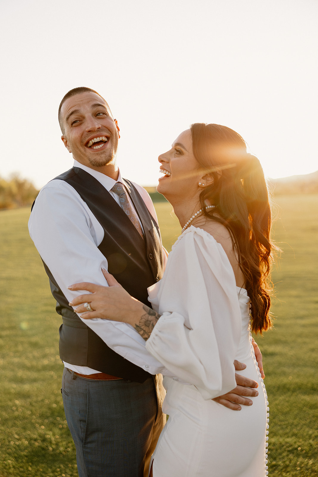 The bride and groom burst into laughter during golden hour portraits, sunlight catching the edge of her veil.