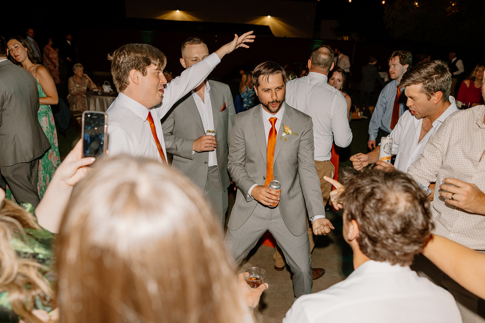 Groom dancing with friends, drink in hand, mid-hype moment on the dance floor.