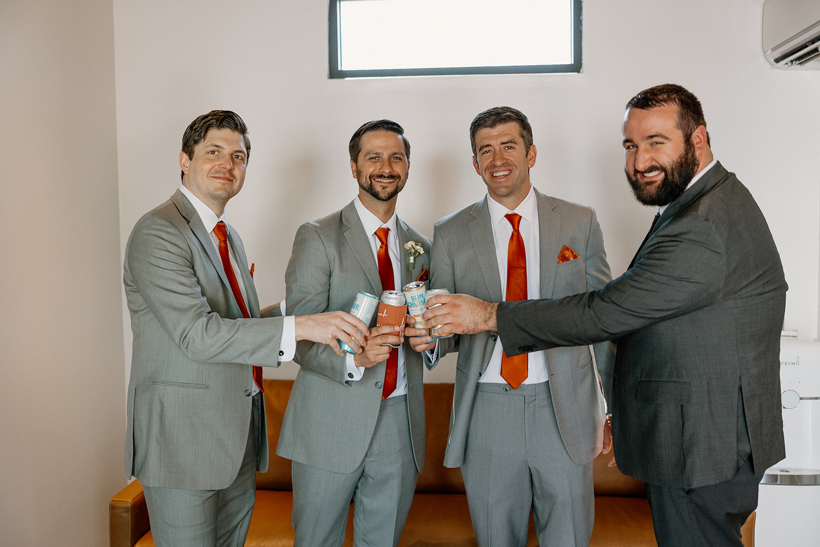Groom and groomsmen clinking canned cocktails in a modern getting-ready suite at The Paseo.