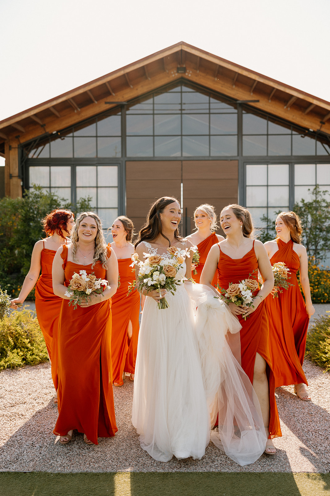The bride and her bridesmaids in matching burnt orange dresses walking outside The Paseo with bright florals and golden light.