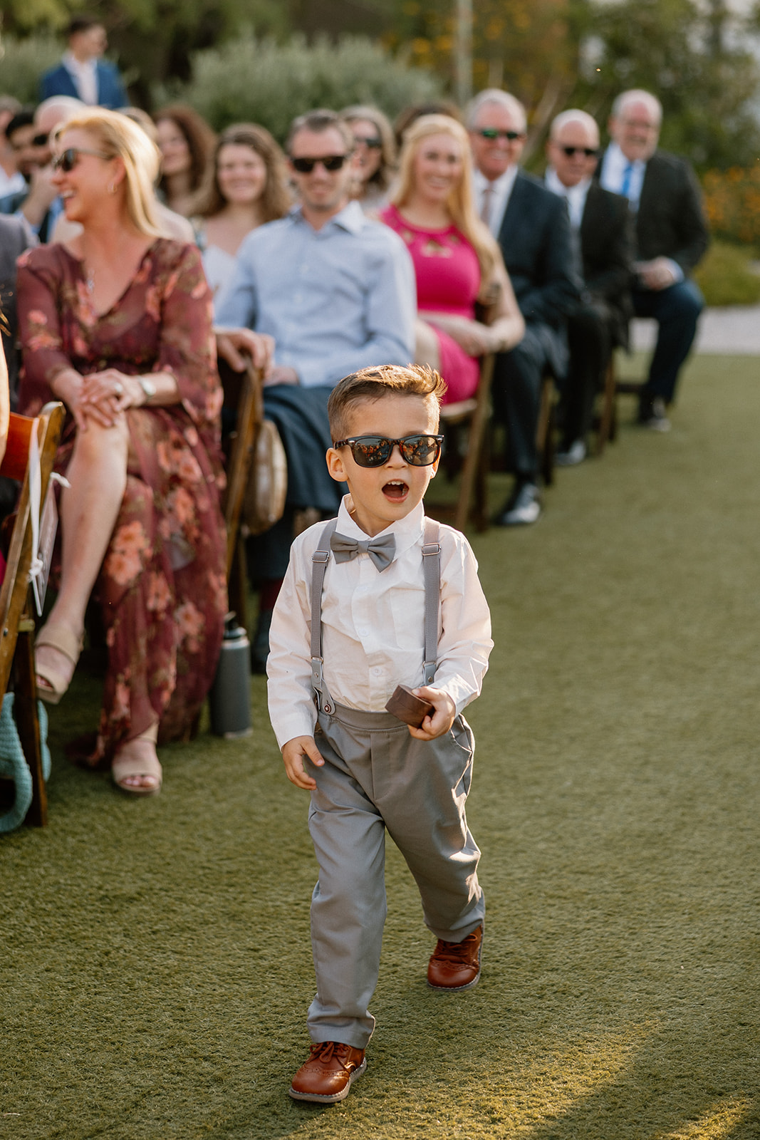 Coolest ring bearer ever strutting down the aisle in sunglasses, totally owning his moment.