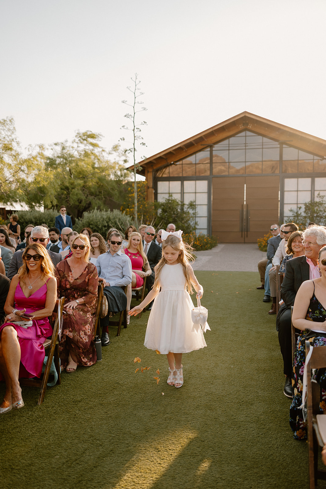 Flower girl walking down the aisle tossing petals with the sun glowing behind her at The Paseo.