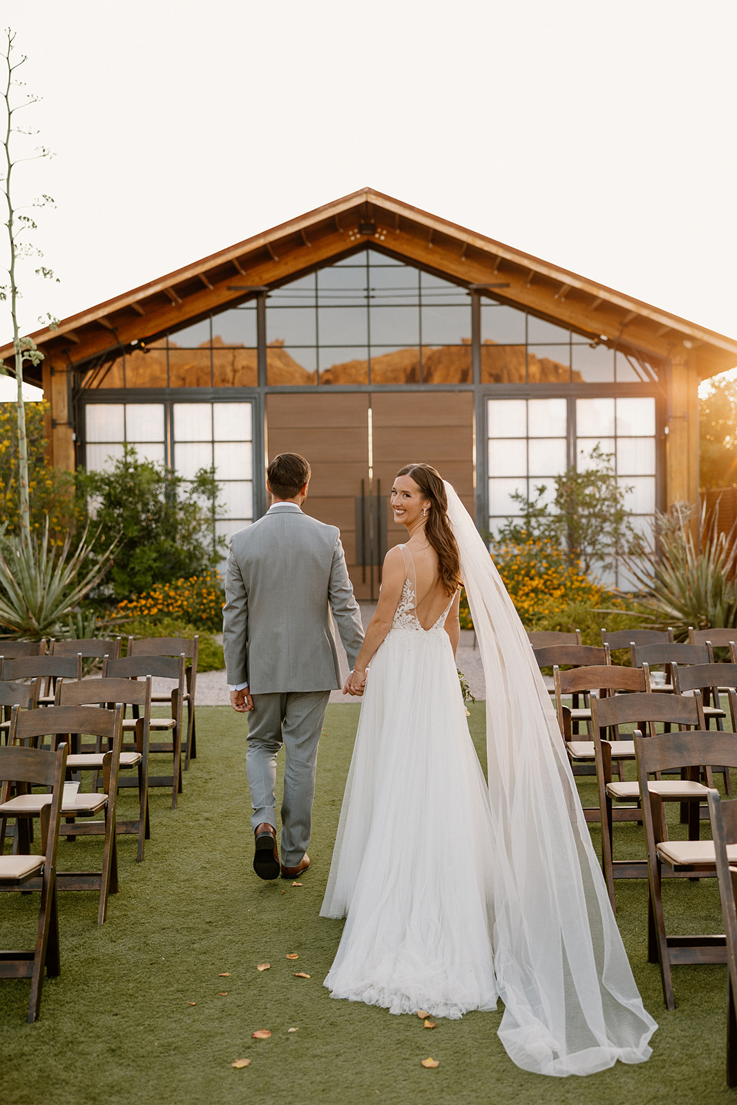 Bride glancing back and smiling as she and her groom walk down the ceremony aisle at The Paseo, golden hour beaming behind them.