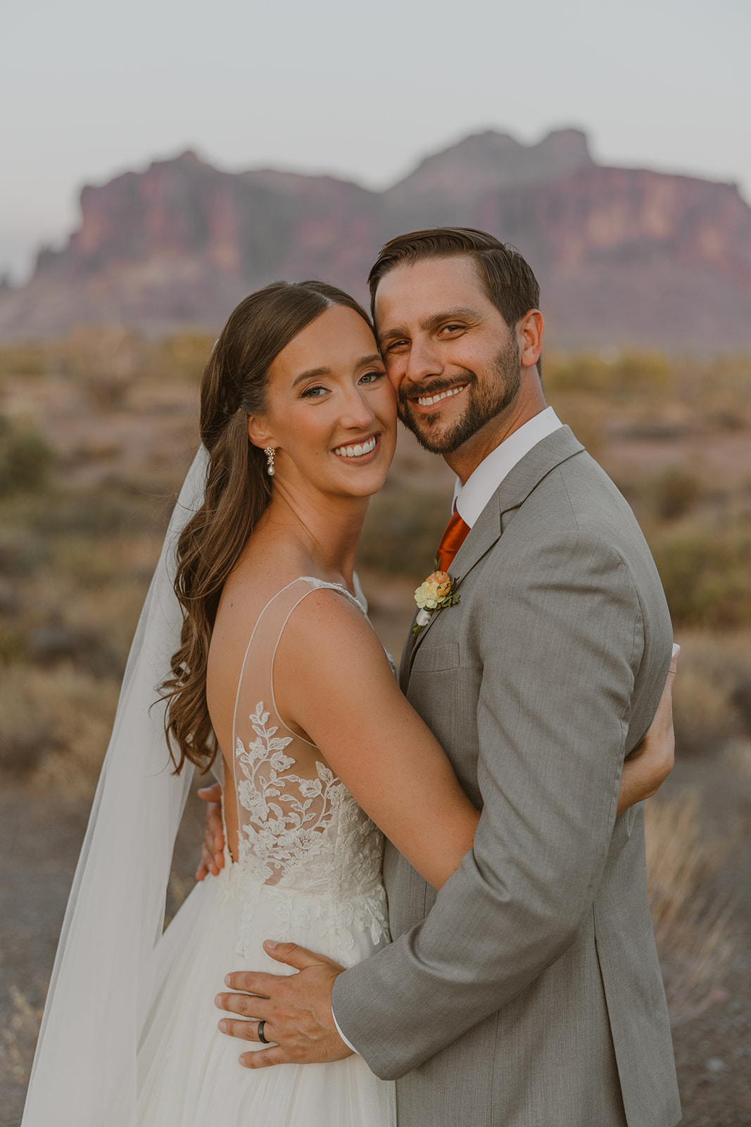 Bride and groom embracing for a sunset portrait with the desert landscape glowing behind them.