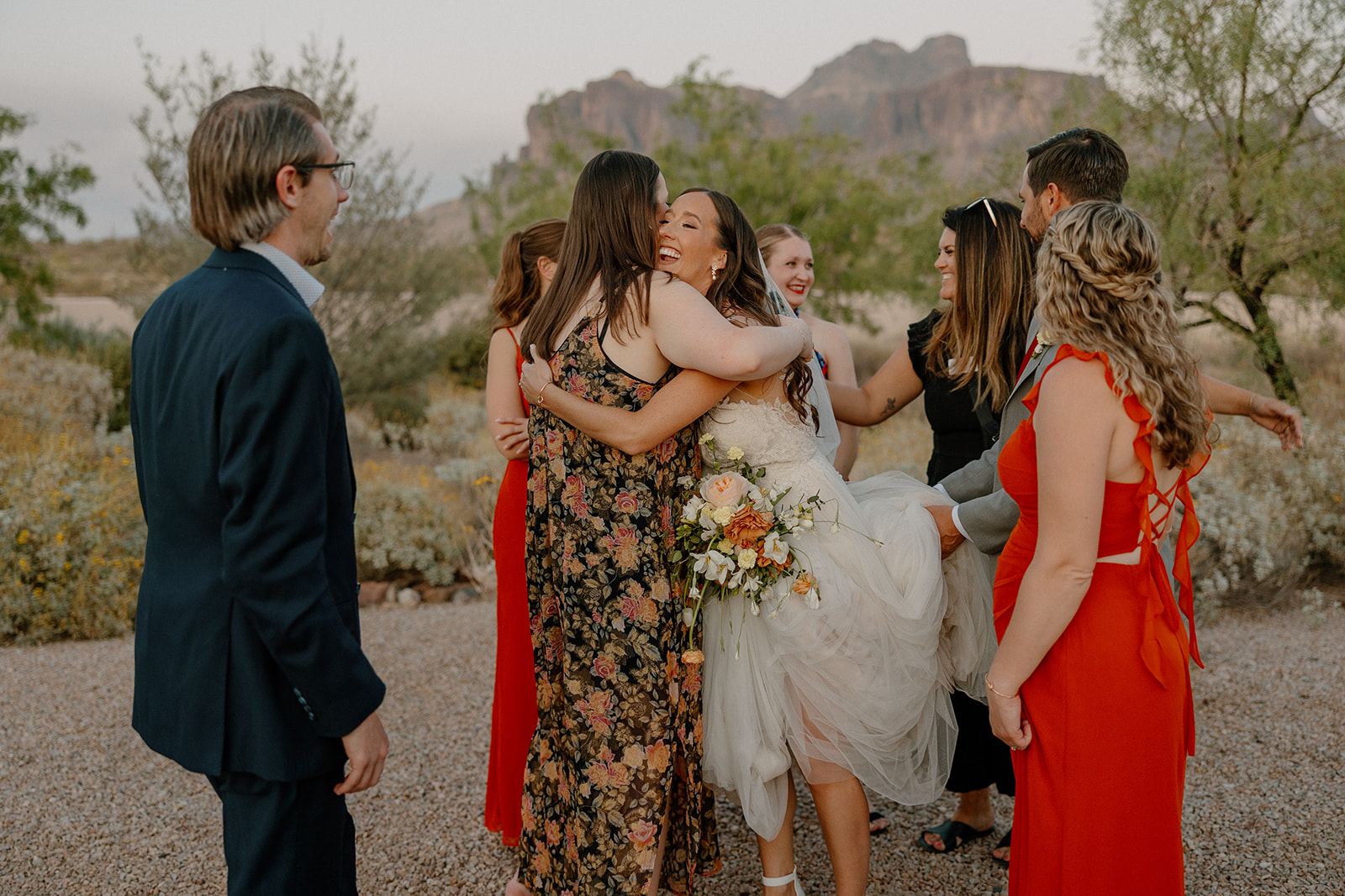 Bride hugging guests during golden hour outside The Paseo, the Superstition Mountains in the background.