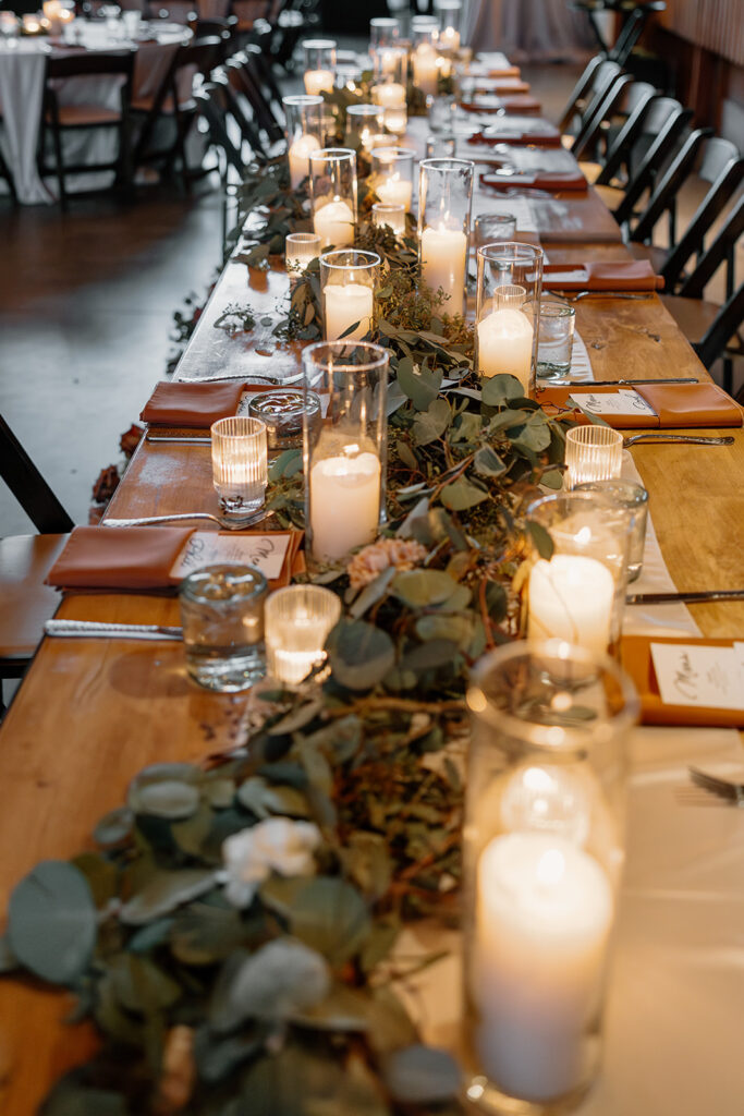 Reception table styled with candles and eucalyptus garland, glowing with cozy, intimate light.