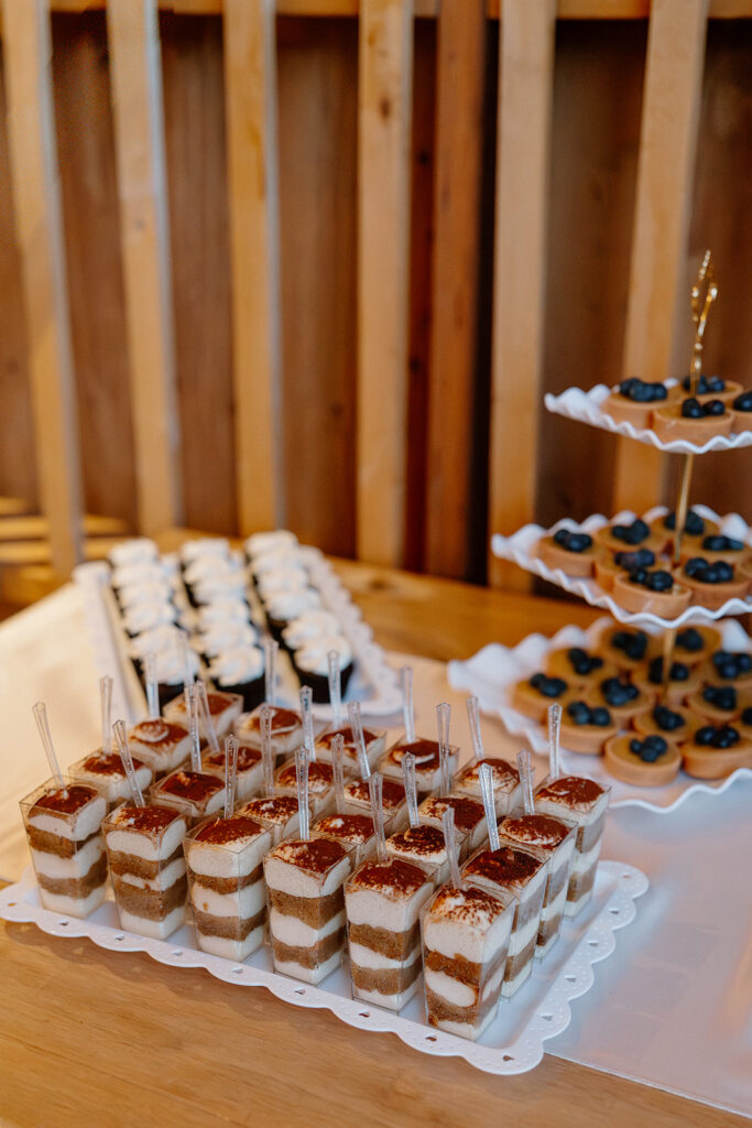 Dessert table stacked with tiramisu shooters, mini cheesecakes, and berry tarts—wedding sweet tooth goals.