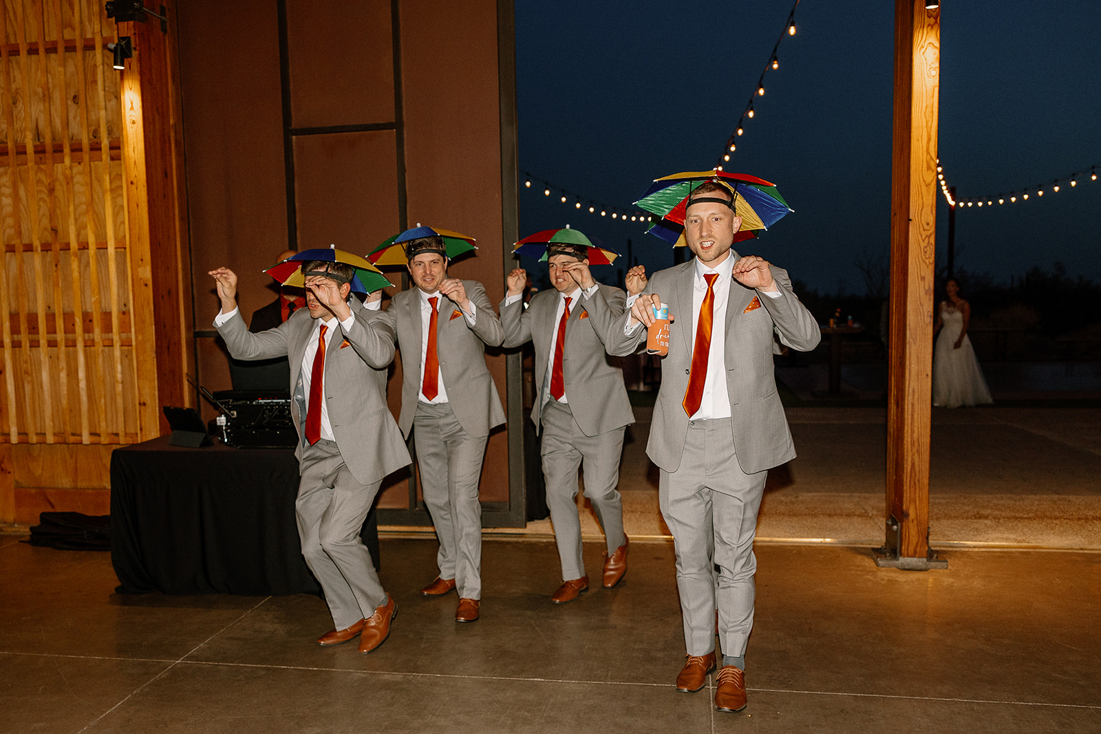 Groomsmen entering the reception at The Paseo wearing rainbow umbrella hats, mid-dance move.