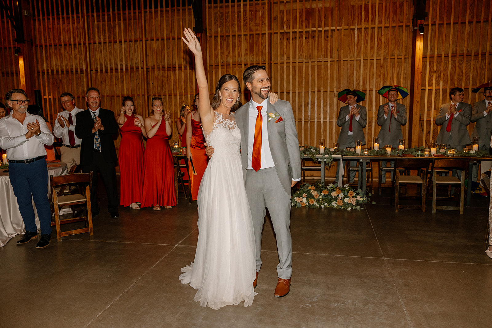 Bride raising her arm in celebration next to the groom as guests cheer around them inside the barn.