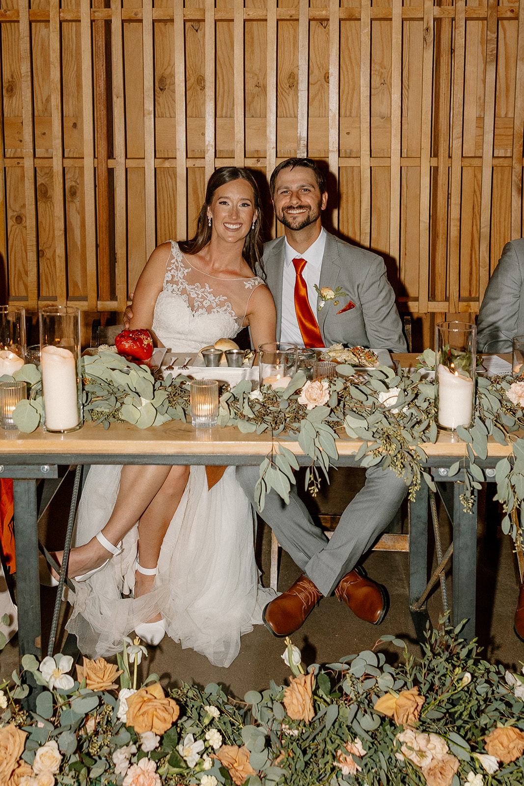 Bride and groom seated at their candlelit sweetheart table surrounded by florals and eucalyptus garlands inside The Paseo.