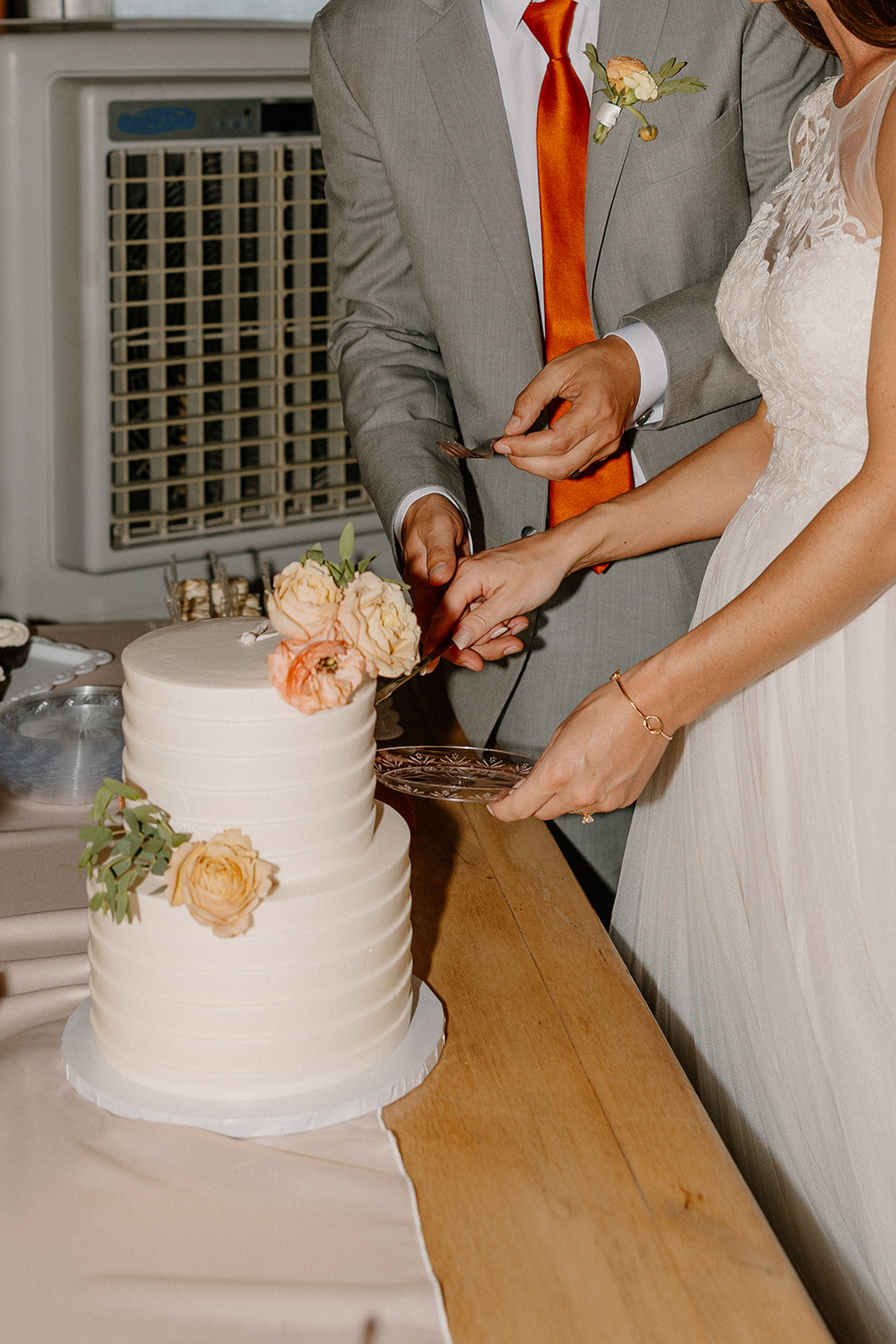 Bride and groom cutting their white tiered wedding cake with soft floral details during the reception at The Paseo.