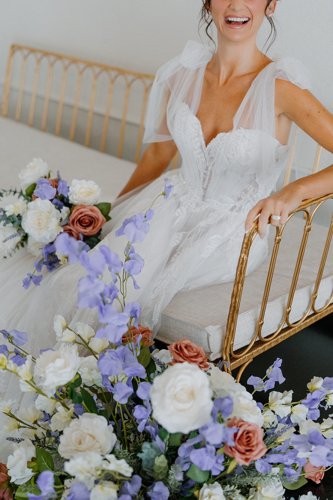 Close-up of the bride smiling with layered florals in blush, ivory, and purple at her feet on the SoHo63 bridal suite floor.
