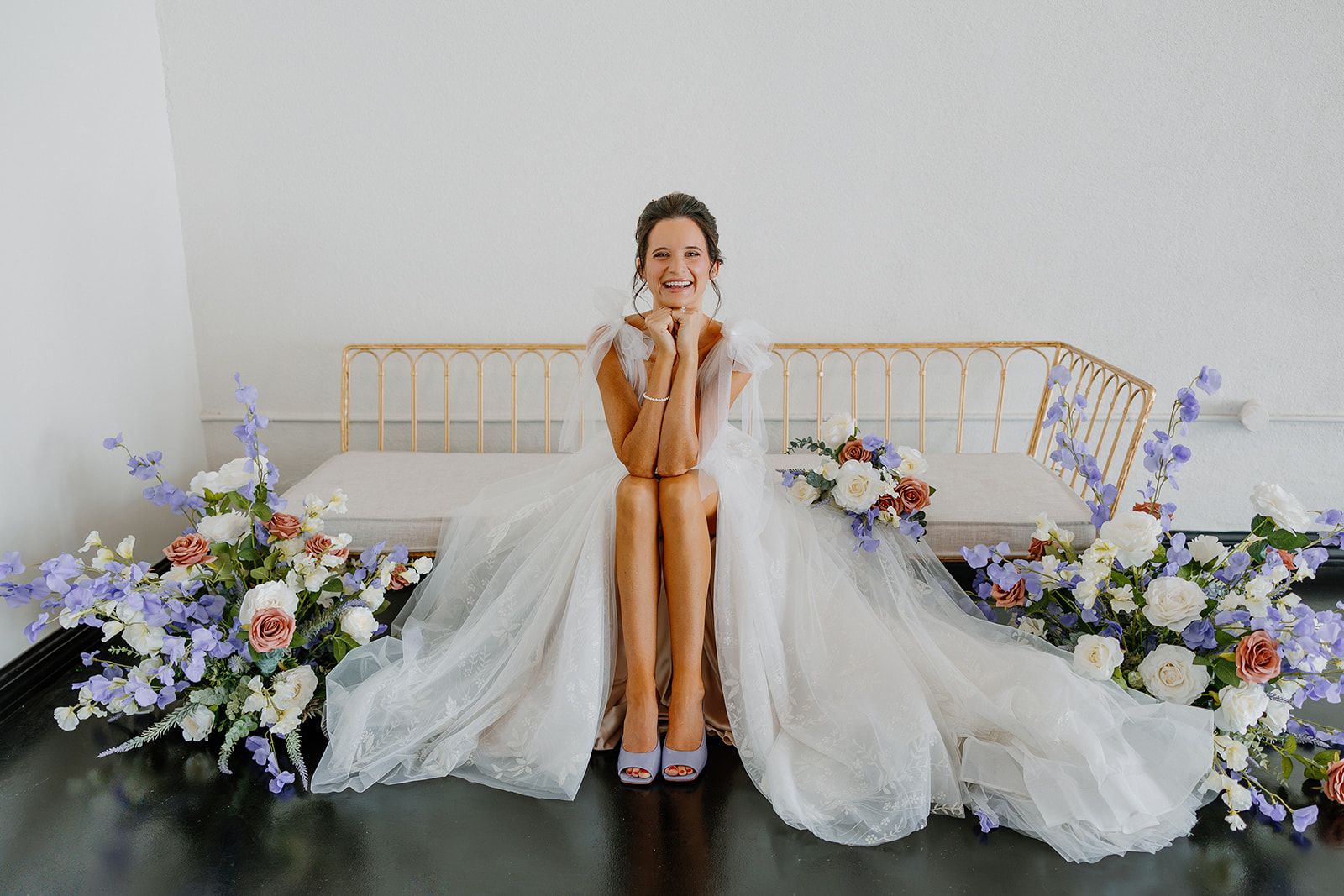 Bride in tulle wedding gown sitting on a modern bench surrounded by lavender, ivory, and terracotta floral arrangements at SoHo63.