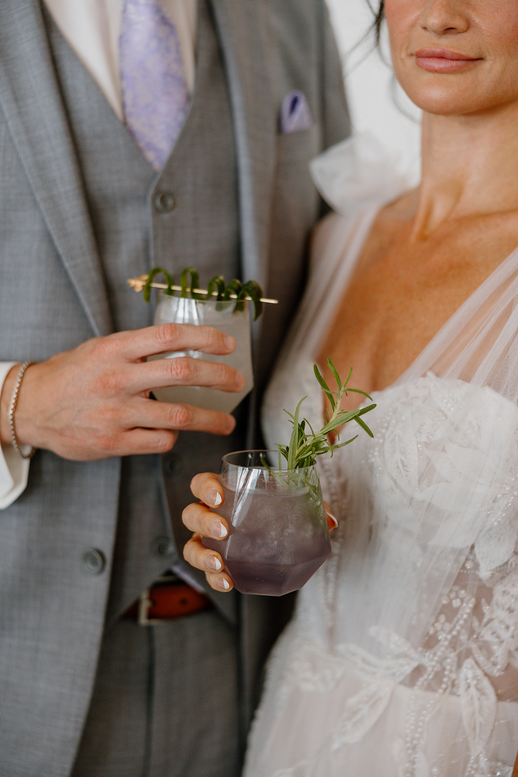Bride and groom holding signature cocktails garnished with rosemary and cucumber at SoHo63 wedding reception.