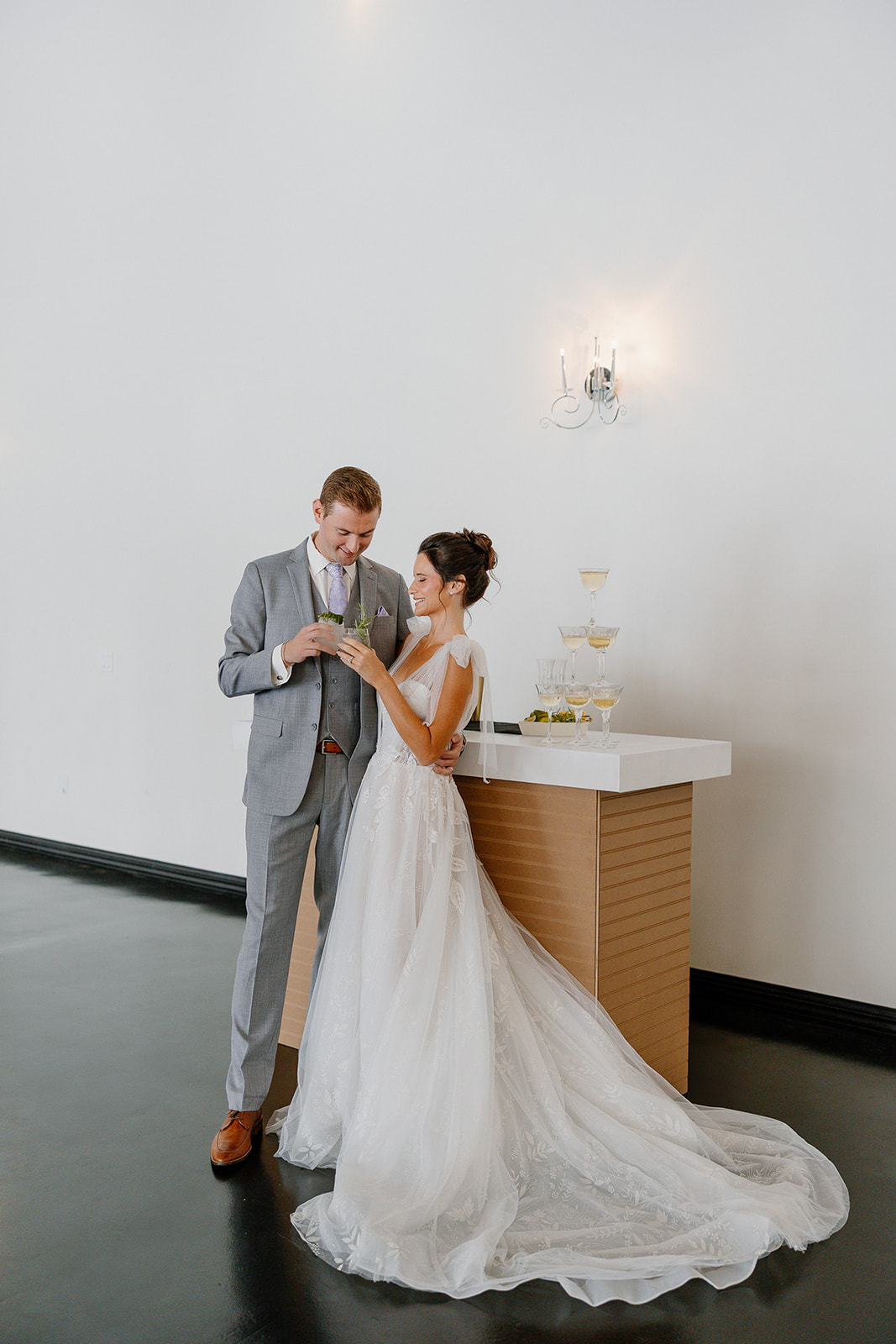 Bride and groom toasting with cocktails beside a modern bar and champagne tower inside SoHo63’s Gramercy Ballroom.