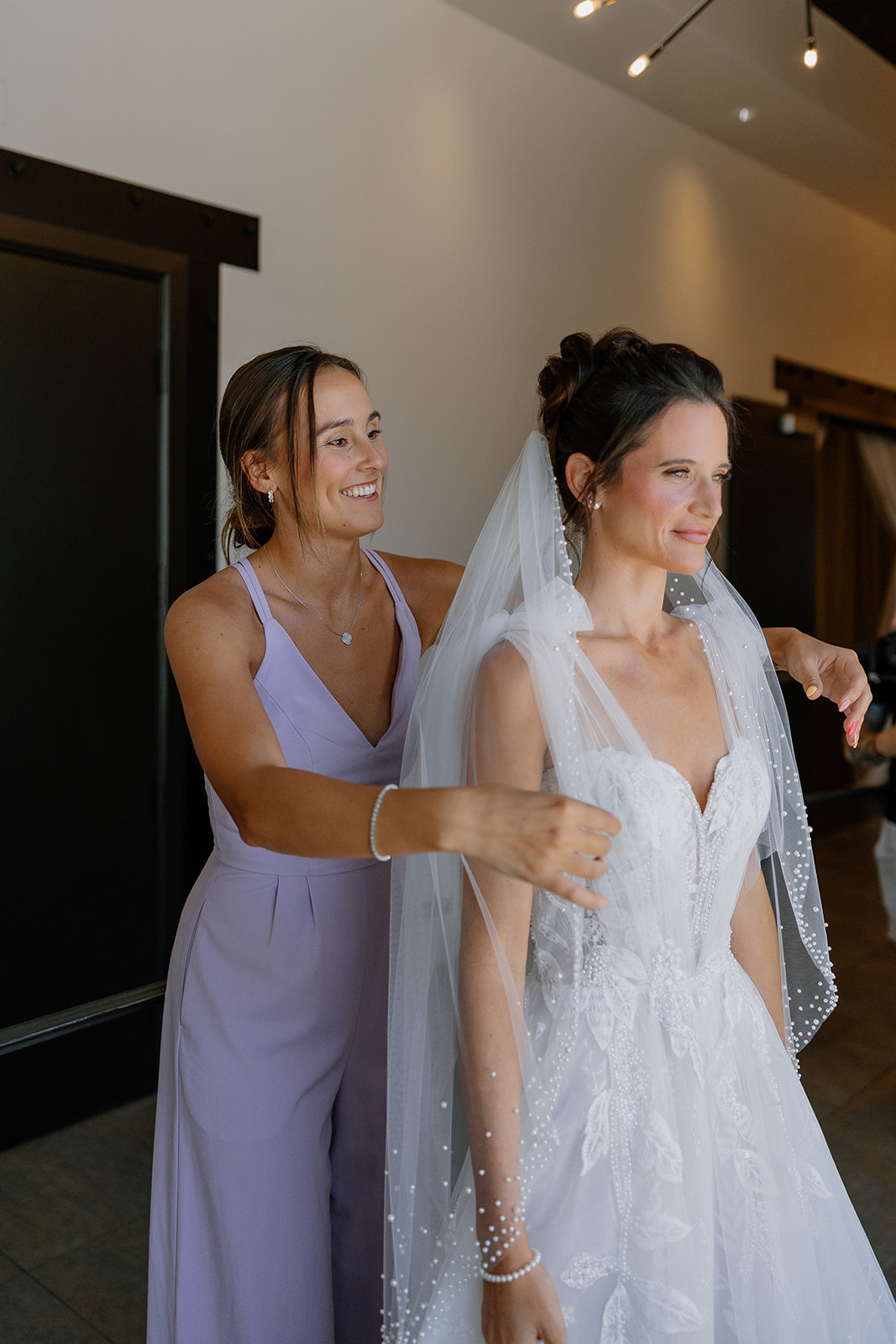 Bridesmaid adjusts the bride’s veil in the getting-ready suite at SoHo63 before the ceremony.