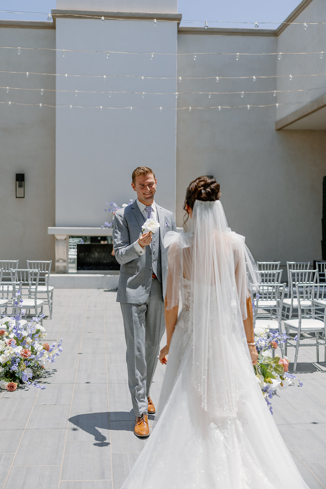 Groom smiles and offers a white rose to his bride during their first look in SoHo63’s Tribeca Terrace ceremony space