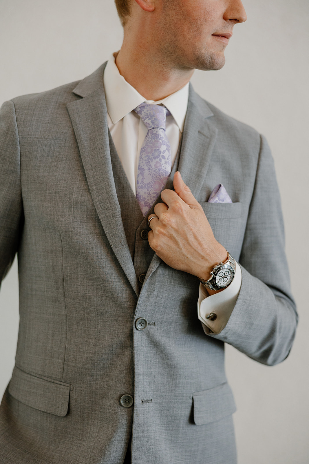 Detail shot of groom’s hand adjusting lavender tie, wearing a gray suit with a classic watch and folded pocket square at SoHo63.