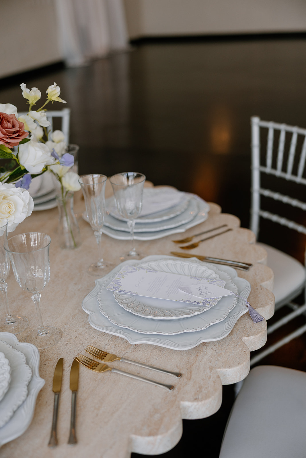 Close-up of scalloped-edge chargers, gold flatware, and lavender-accented menus on a wedding reception table at SoHo63.