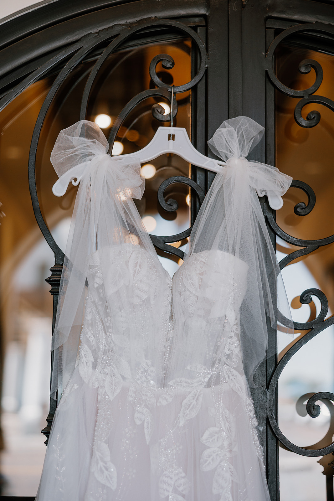 Detailed bridal gown with embroidered lace and tulle bows hanging on a decorative iron door at SoHo63.