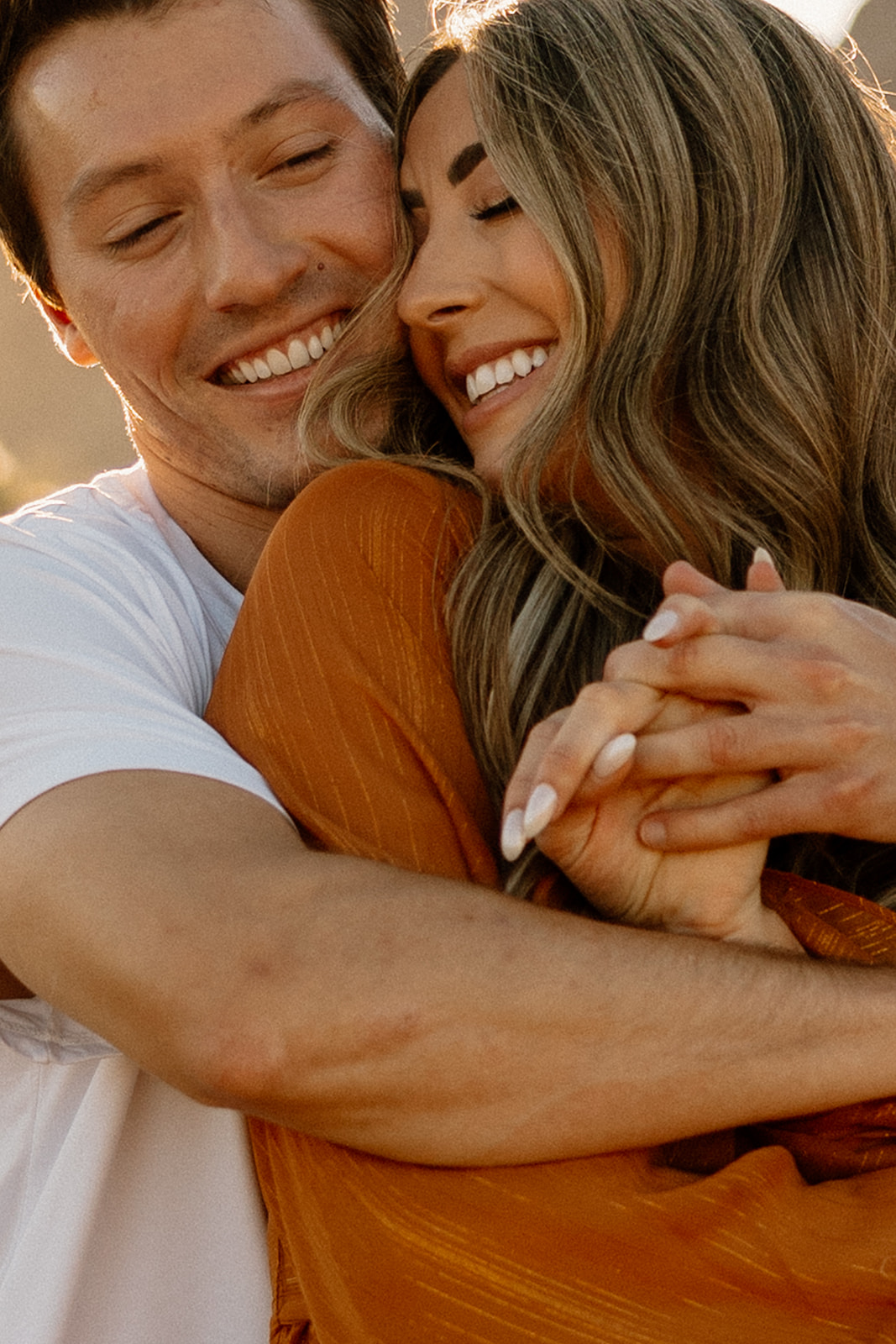 Close-up of a joyful couple holding hands and smiling, the woman’s engagement ring catching the light.