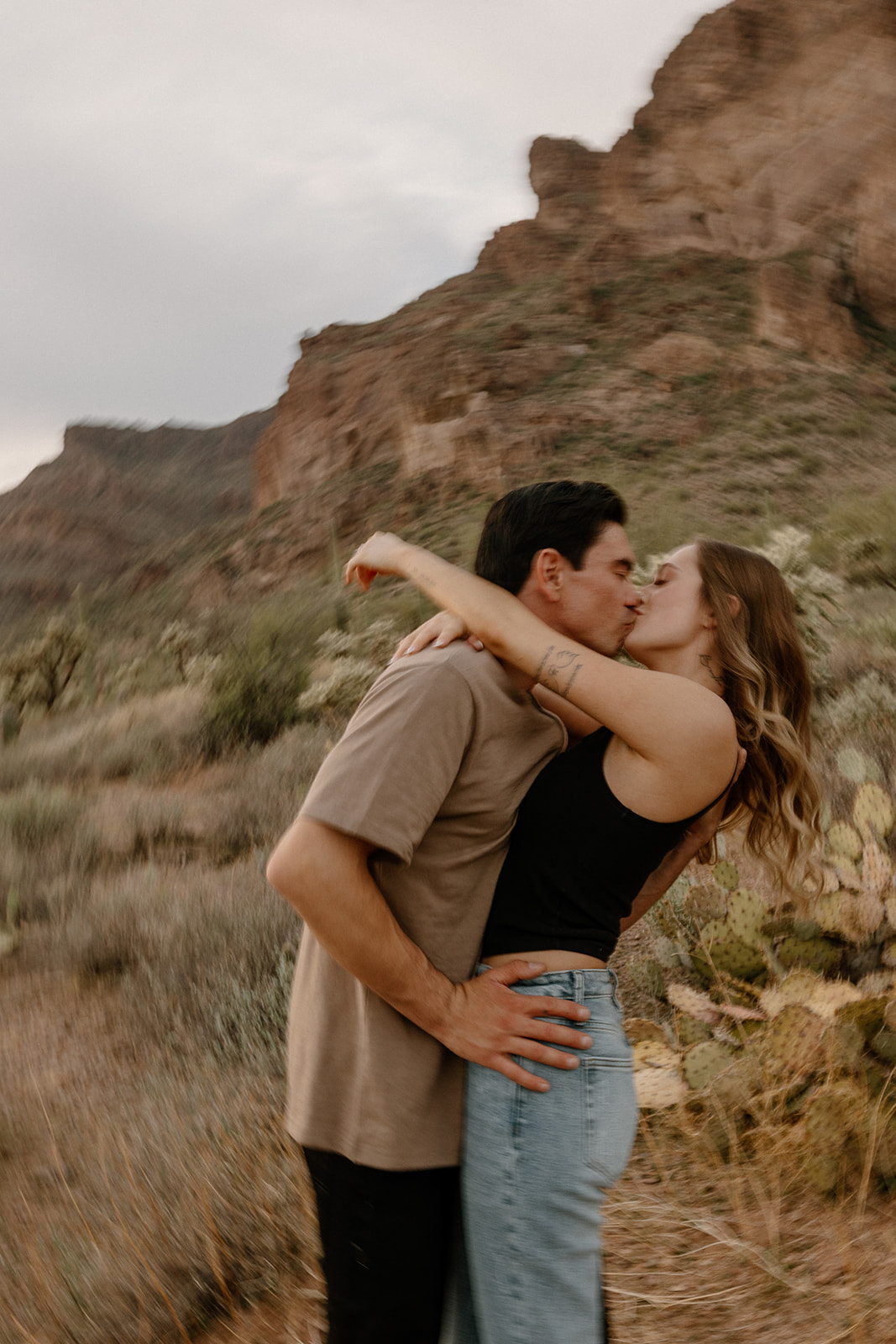 Blurry, candid kiss shared by a couple mid-laugh among the wild cacti and earth tones of the Arizona desert.