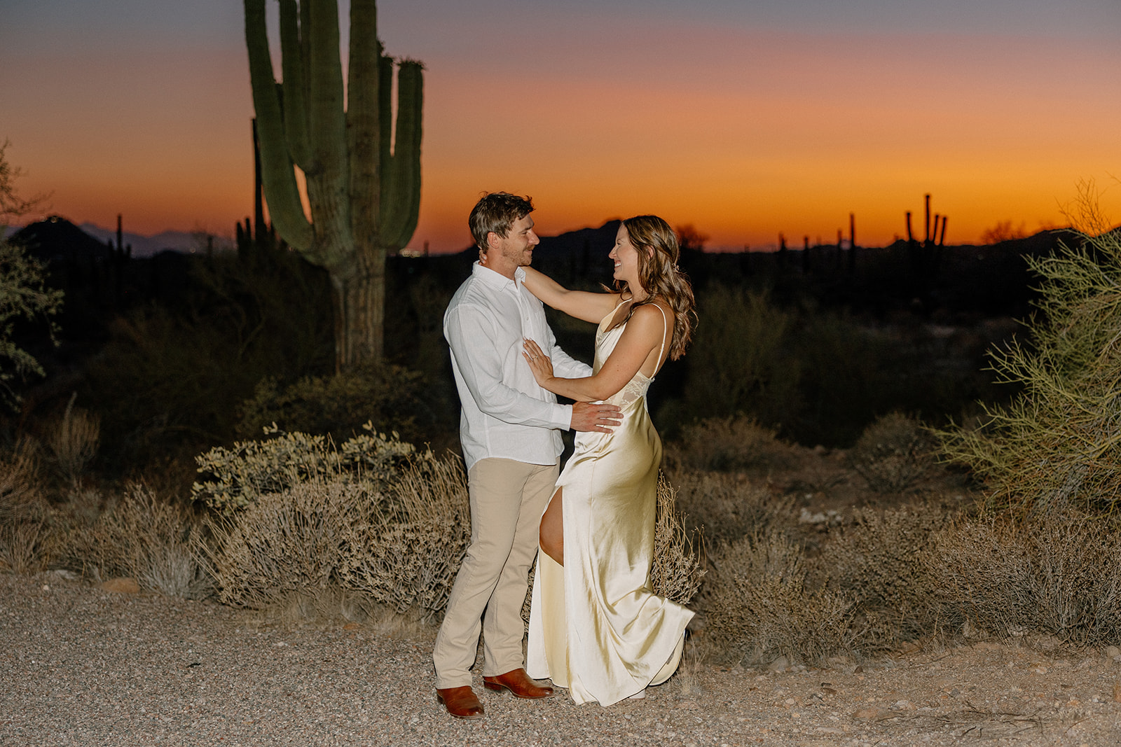 Elegant couple dancing in the desert at twilight, with towering saguaros and golden-hour light glowing behind them.