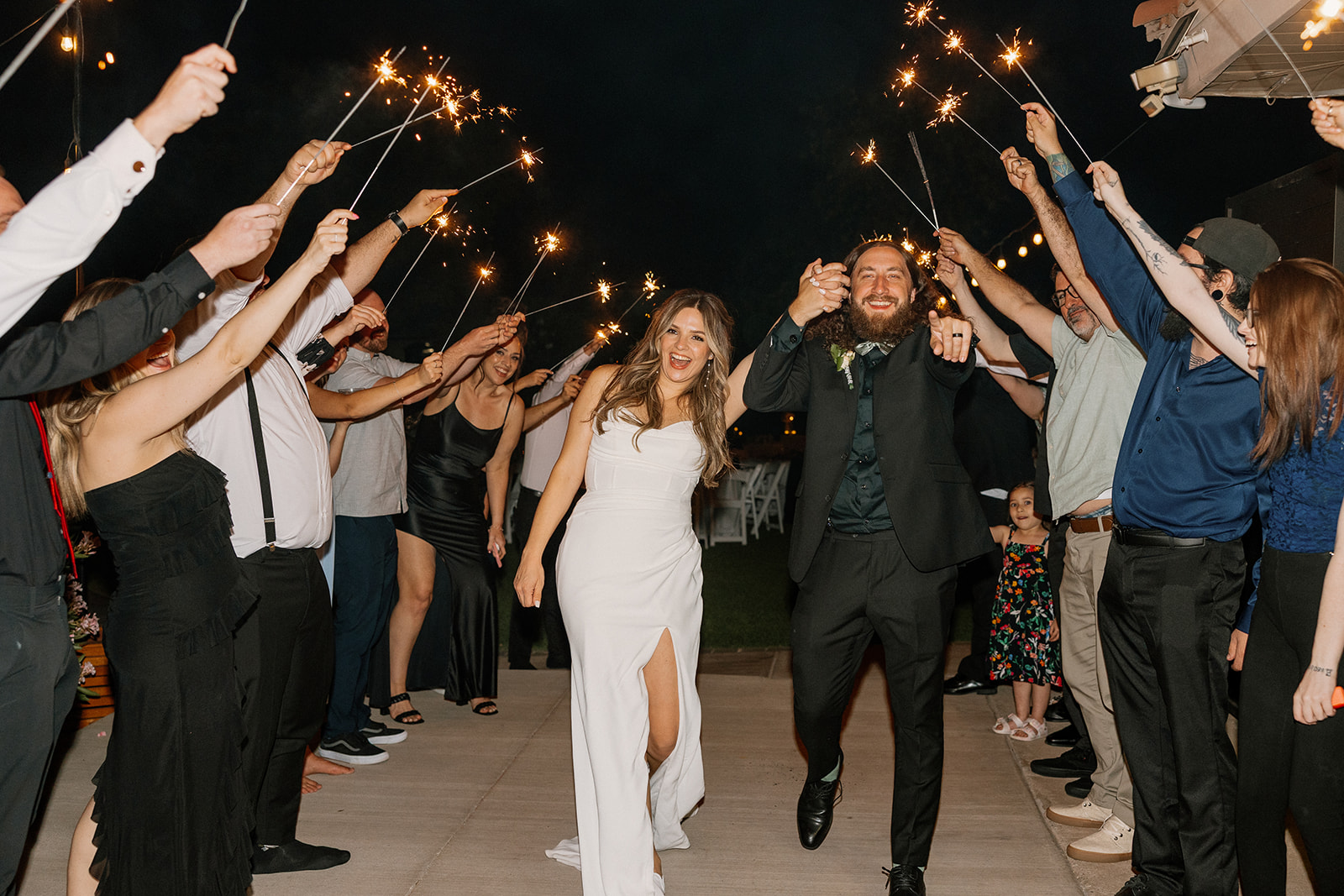 Newlyweds celebrate with a joyful sparkler exit, surrounded by cheering guests outside an Arizona wedding venue.