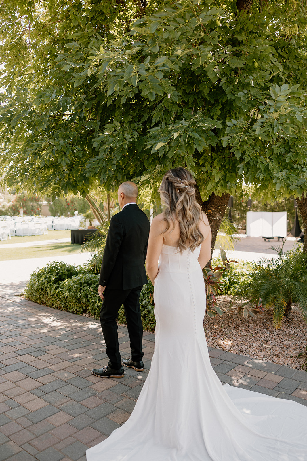A bride approaches her father for a first look, her train trailing behind her on the brick path.