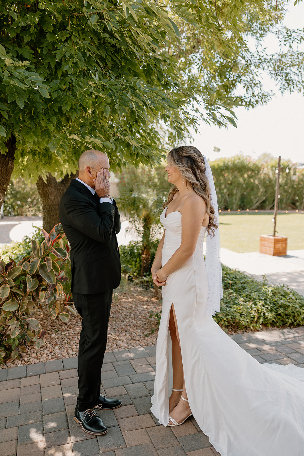 An emotional first look between the bride and her father, both holding back tears beneath the trees.