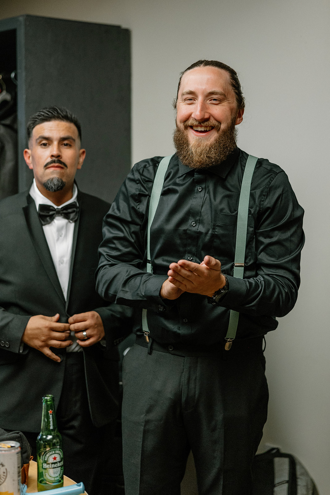 The groom claps with excitement as he finishes getting dressed, suspenders on and ready to go.