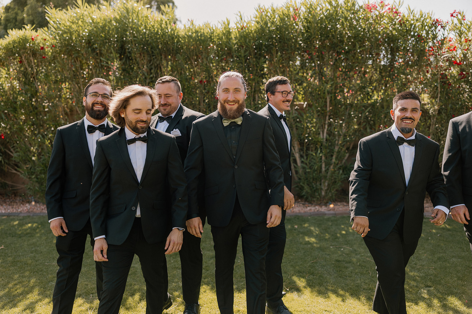 Groom and his groomsmen walk confidently across the lawn, dressed in sharp black tuxedos at an Arizona wedding venue.