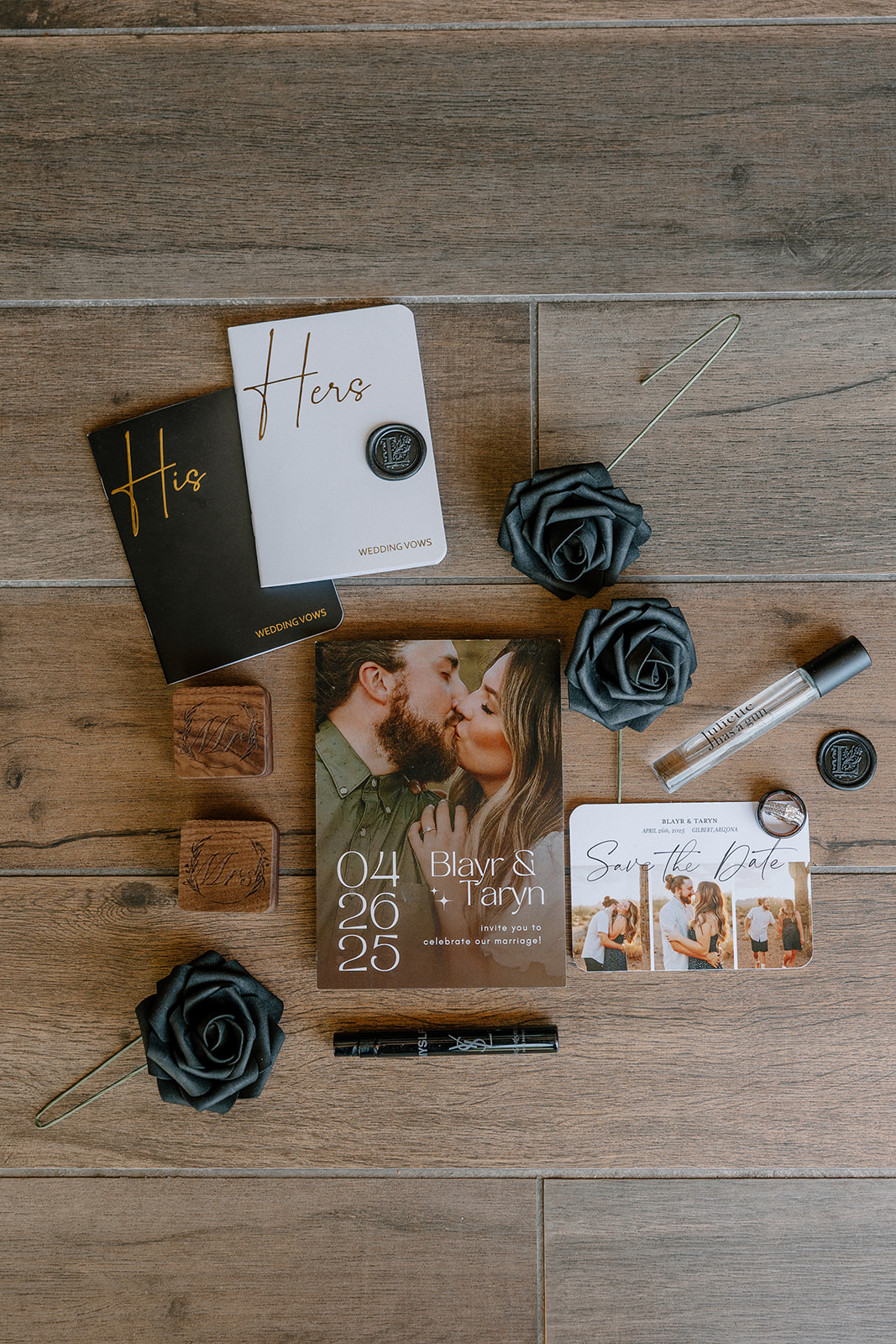 Flat lay of wedding details including vow books, wax seals, a save-the-date card, and black paper flowers.