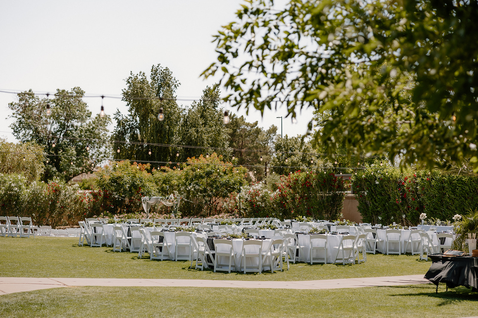 A wide view of the outdoor reception setup shows round tables and string lights on the lawn of an Arizona wedding venue.