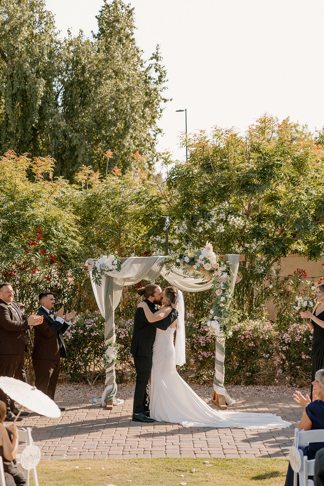 Bride and groom share their first kiss as a married couple under a romantic floral arch at their Arizona wedding venue.