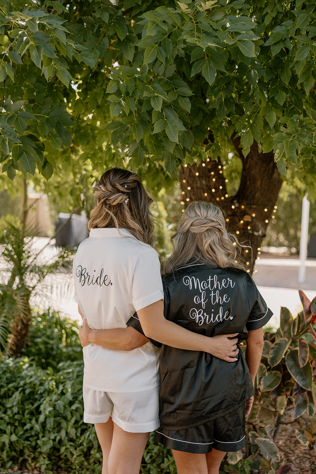 With arms around each other, the bride and her mom share a quiet moment in matching “Bride” and “Mother of the Bride” pajama sets.