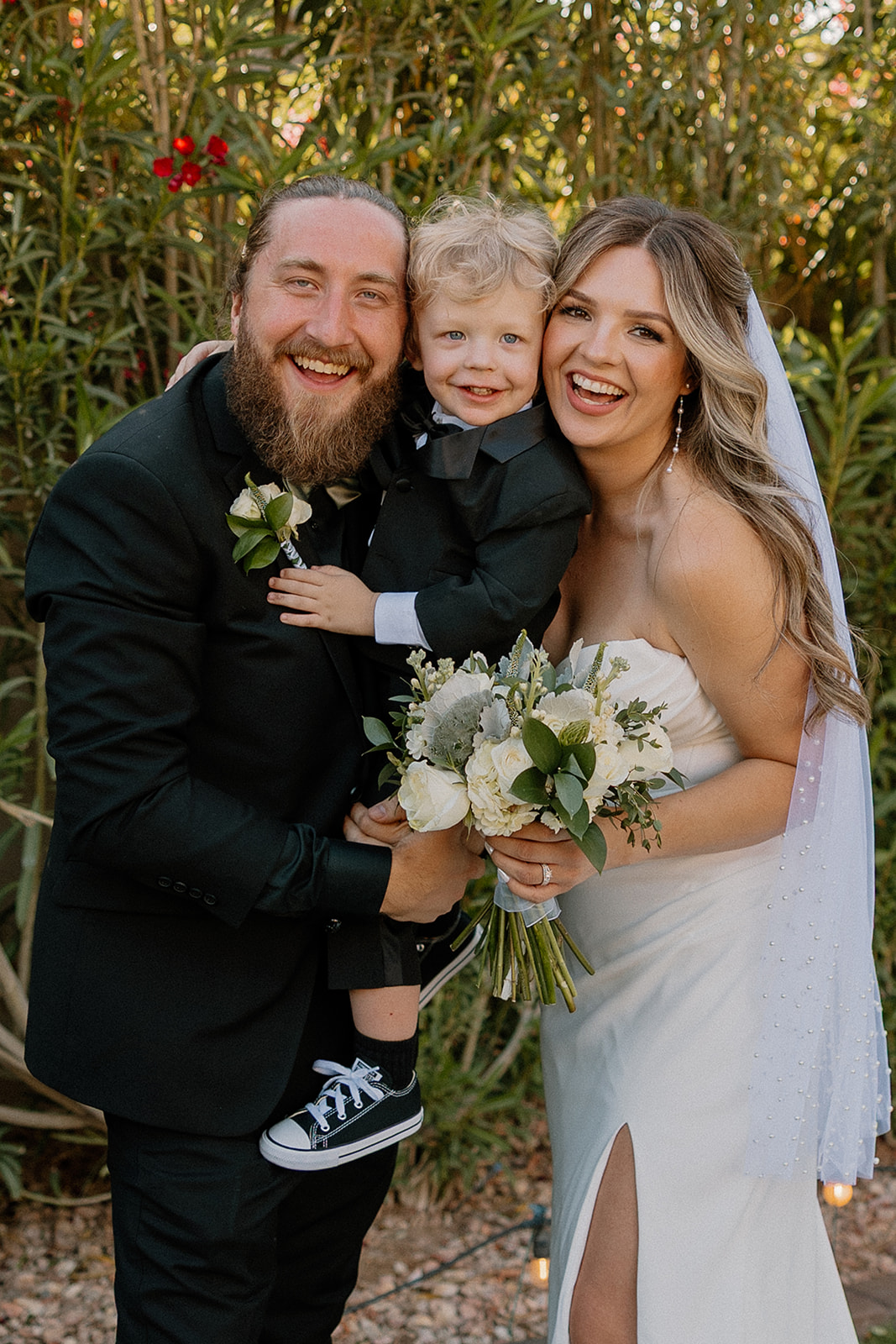 The bride and groom hold their son between them for a sweet, candid family portrait in matching formalwear.