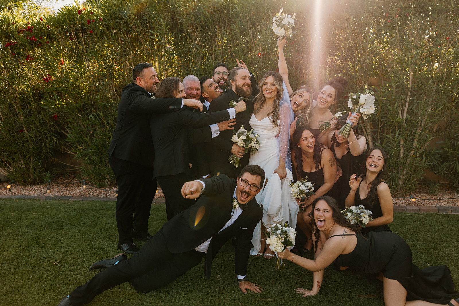 The full wedding party piles in for a playful group photo full of energy and celebration at an Arizona wedding venue.
