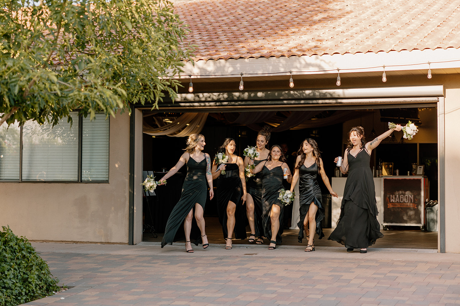 The bridesmaids strut into the party in bold black dresses, bouquets in hand, fully living the moment.