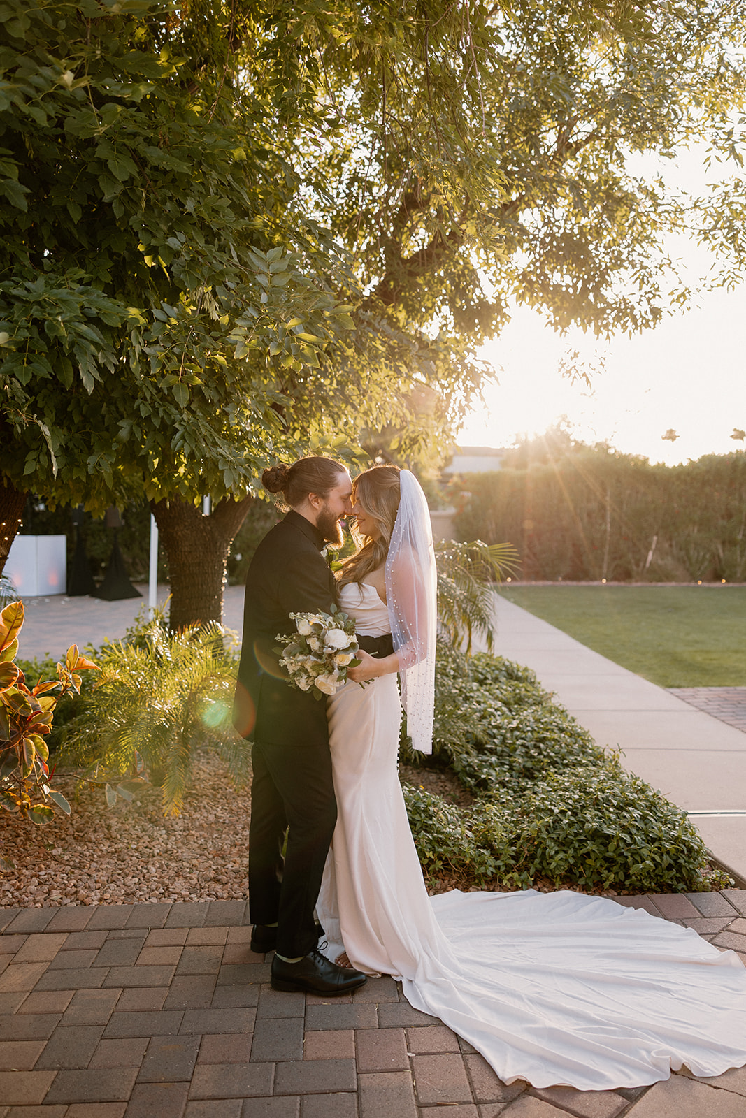 Golden hour glows behind the couple as they hold each other on a shaded brick path outside their Arizona wedding venue.