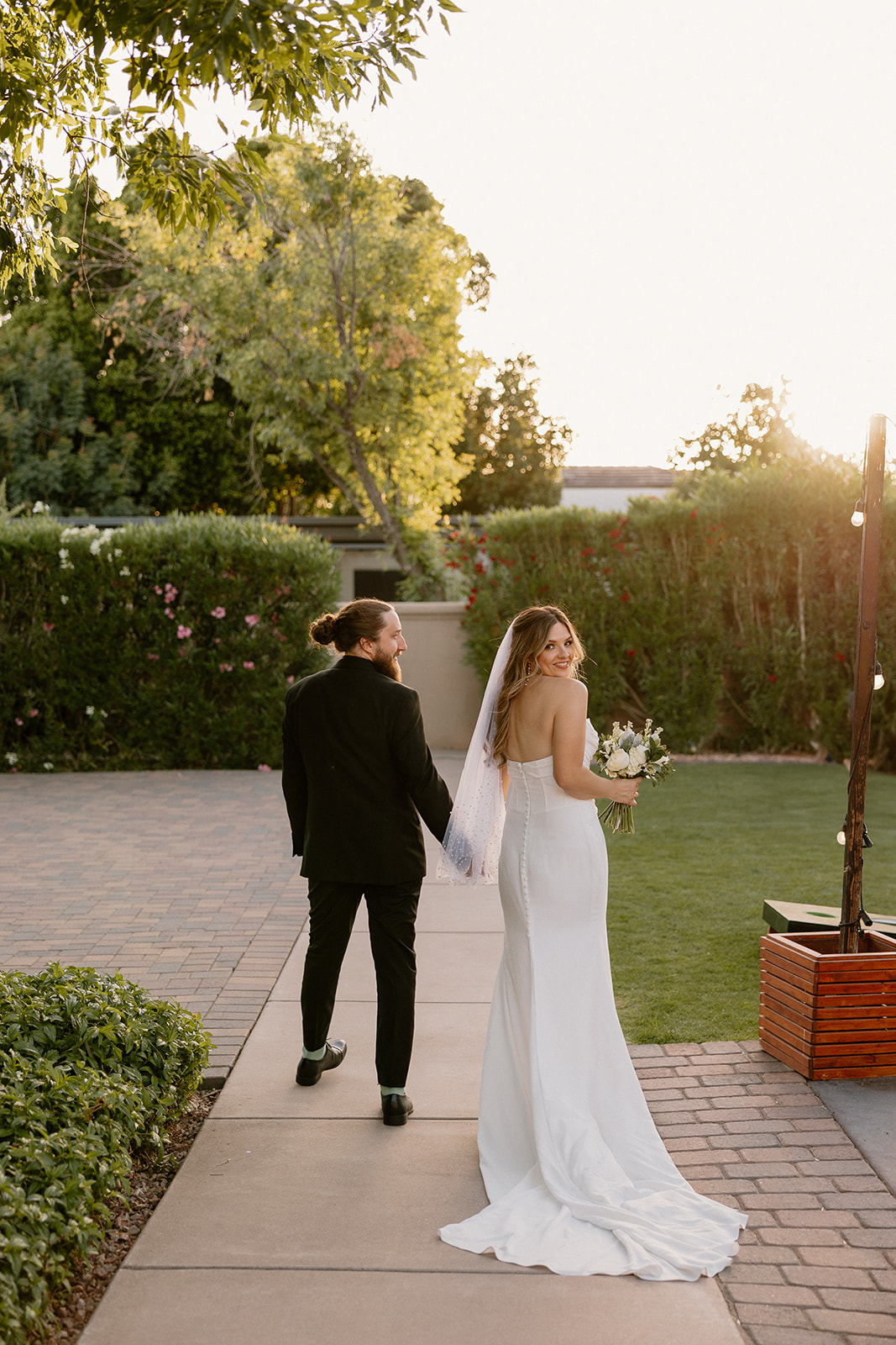 Bride turns back with a smile while walking hand-in-hand with the groom at an Arizona wedding venue during golden hour.