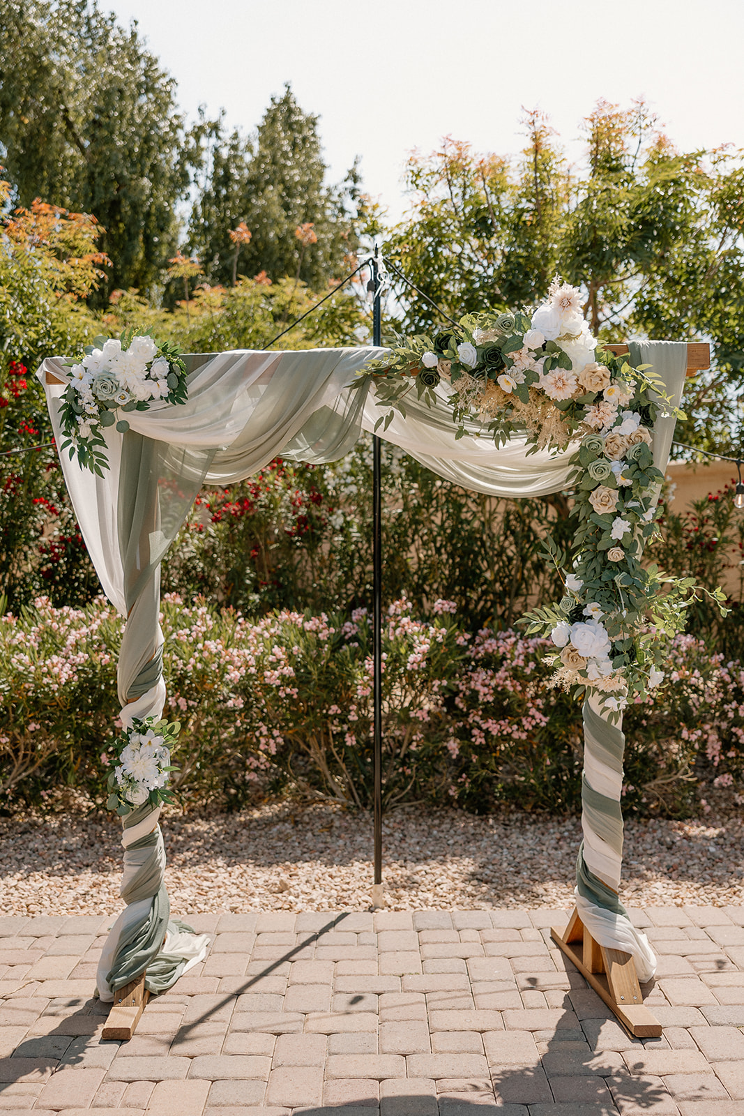 An elegant wedding arch draped in white and sage fabric, adorned with lush florals, stands ready for the ceremony.