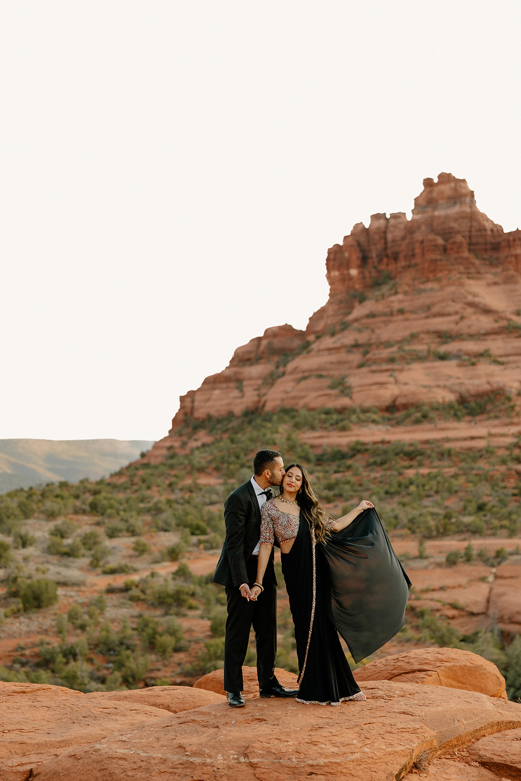 Formal dressed couple holding hands while man kisses woman's forehead during Sedona elopement ceremony