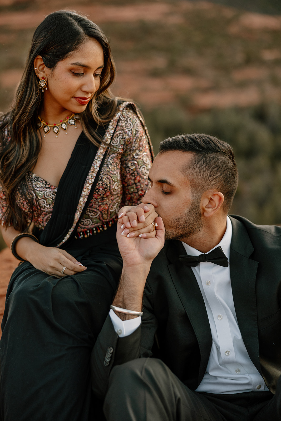 He kisses her hand while she looks down lovingly, dressed in a sequined blouse and black saree.
